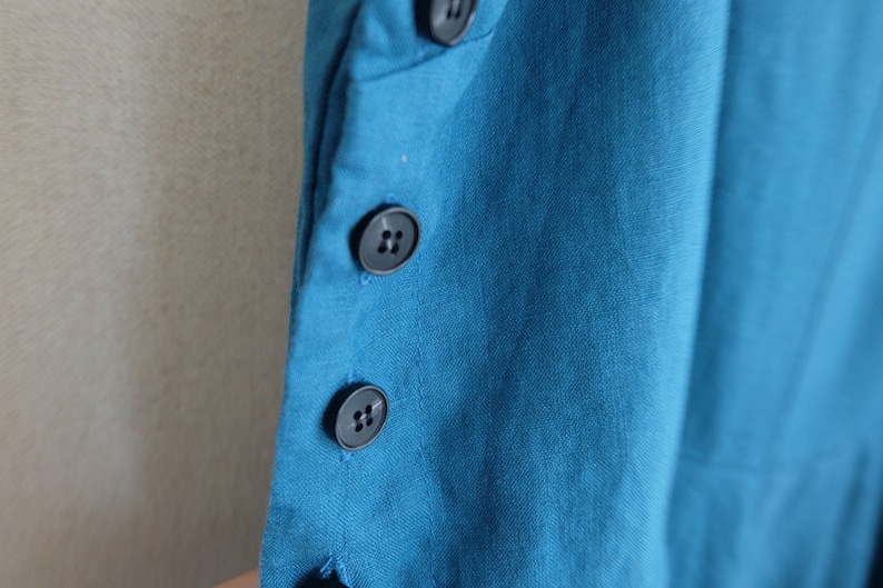 May include: A close-up of a teal blue fabric with four black buttons. The buttons are sewn on the fabric in a vertical line.