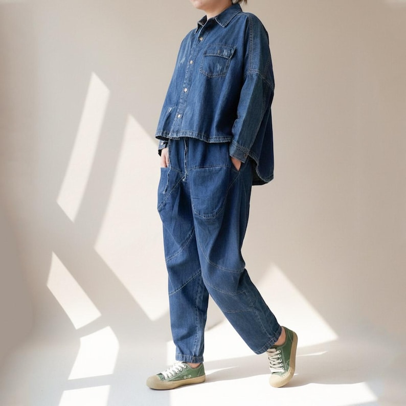May include: A denim two-piece outfit, featuring a button-down shirt and matching pants. The shirt has two chest pockets. The pants have large front pockets and a relaxed fit. The outfit is a medium blue color and is paired with green canvas sneakers.