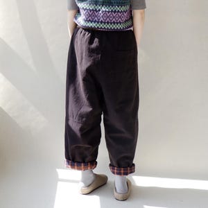 May include: Brown corduroy pants with a plaid cuff. The pants have a drawstring waist and a relaxed fit.