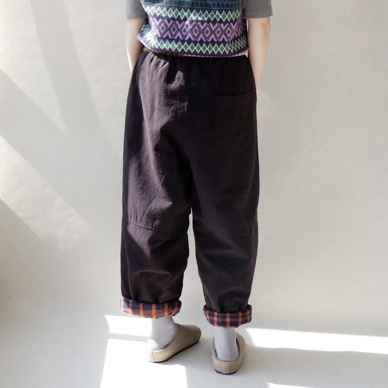 May include: Brown corduroy pants with a plaid cuff. The pants have a drawstring waist and a relaxed fit.