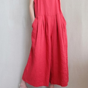 May include: A red linen jumpsuit with wide legs and a square neckline. The jumpsuit has two large pockets on the front and thin straps.