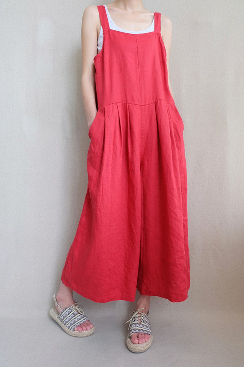 May include: A red linen jumpsuit with wide legs and a square neckline. The jumpsuit has two large pockets on the front and thin straps.