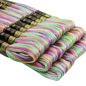 Puede incluir: Primer plano de ocho carretes de hilo de bordar multicolor. El hilo es una mezcla de rosa, verde, morado y amarillo. Cada carrete está etiquetado con el texto "133" y "8m".