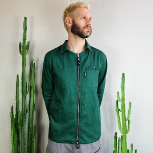 Puede incluir: Una chaqueta de trabajo verde oscuro con cierre de cremallera y varios bolsillos. La chaqueta está hecha de una tela resistente y tiene un corte holgado.
