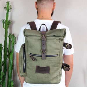 May include: A green canvas backpack with brown leather straps and buckles. The backpack has a roll-top closure and a small patch with the text "JUNTAL PROJECTS" on the front.