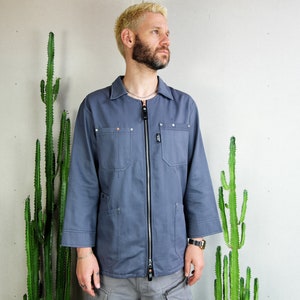 Può includere: Una giacca da lavoro blu con chiusura a zip e diverse tasche. La giacca ha una vestibilità rilassata ed è realizzata in un tessuto resistente.