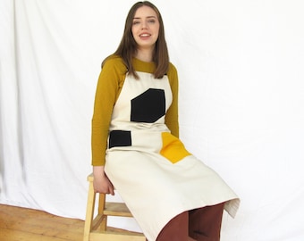 Delantal de lona para estudio: espalda cruzada ajustable, bolsillos negros y amarillos.