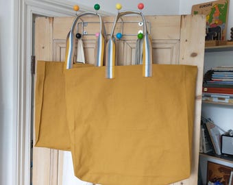 Bolsas grandes de lona con asas a rayas hechas con retales reciclados de lona de color amarillo ocre.