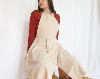 Delantal de alfarería de algodón orgánico con falda plisada de pierna dividida, bolsillo en el babero y bolsillos en la falda.