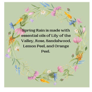 May include: A watercolor illustration of a floral wreath in shades of pink, orange, blue, and white, encircling text that reads "Spring Rain is made with essential oils of Lily of the Valley, Rose, Sandalwood, Lemon Peel, and Orange Peel."