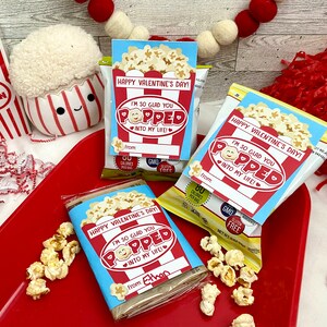 Puede incluir: Tres bolsas de palomitas de maíz con etiquetas de regalo con temática del Día de San Valentín. Las etiquetas muestran un cubo de palomitas de maíz de dibujos animados con una cara sonriente y el texto "¡Me alegro tanto de que hayas llegado a mi vida!"