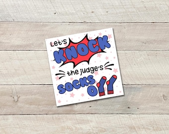 May include: A square card featuring the phrase "Let's KNOCK the judge's SOCKS off" in a comic book style. The words "KNOCK" and "SOCKS" are in blue, outlined in white, with a red burst behind "KNOCK". Two blue socks with red stripes are at the bottom.