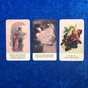 K&ouml;nnte beinhalten: Drei Tarotkarten mit Illustrationen und Text. Die erste Karte zeigt eine Frau, die unter einem Halbmond steht, mit dem Text "H&ouml;re auf deine intuitiven Signale, sie sind real. Und sie werden dich in die richtige Richtung f&uuml;hren.". Die zweite Karte zeigt eine Frau, die eine Handvoll Sterne h&auml;lt, mit dem Text "Nur in der Dunkelheit k&ouml;nnen wir die Sterne sehen". Die dritte Karte zeigt eine Fee, die auf einer roten Rose sitzt, mit dem Text "Es ist in Ordnung, sich Zeit zu nehmen."