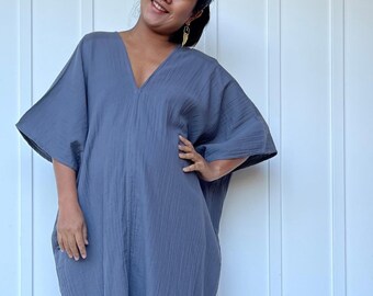 May include: A long, flowing, slate-blue dress with a V-neck and wide sleeves. The dress has side slits and is made of a soft, textured fabric. The text "MALA handworks Hollywood, MD" is printed on the dress.