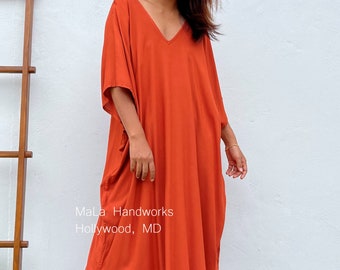 Puede incluir: Un vestido largo, de color óxido, holgado, con cuello en V y aberturas laterales. El vestido está hecho de una tela suave y fluida. Mala Handworks Hollywood, MD está impreso en el vestido.