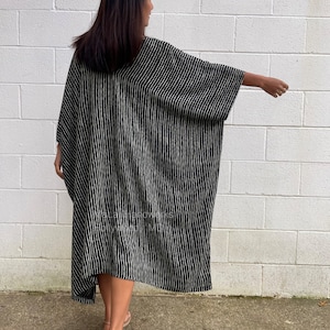 K&ouml;nnte beinhalten: Ein schwarz-wei&szlig; gestreiftes Maxikleid mit einer langen, flie&szlig;enden Silhouette. Das Kleid hat einen V-Ausschnitt und Dreiviertel&auml;rmel. Das Model tr&auml;gt das Kleid mit Sandalen.