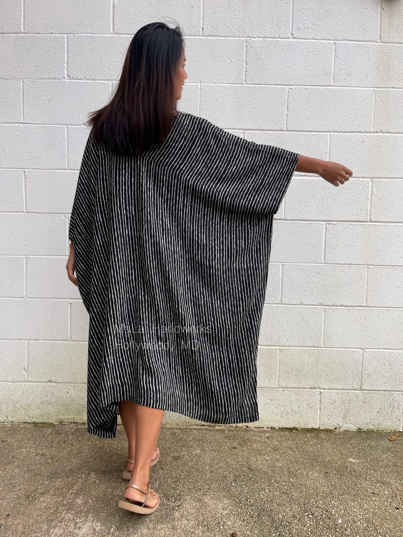 K&ouml;nnte beinhalten: Ein schwarz-wei&szlig; gestreiftes Maxikleid mit einer langen, flie&szlig;enden Silhouette. Das Kleid hat einen V-Ausschnitt und Dreiviertel&auml;rmel. Das Model tr&auml;gt das Kleid mit Sandalen.
