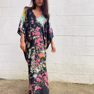 May include: A long black maxi dress with a tie-dye pattern in shades of pink, blue, and yellow. The dress has a V-neck and a relaxed fit.