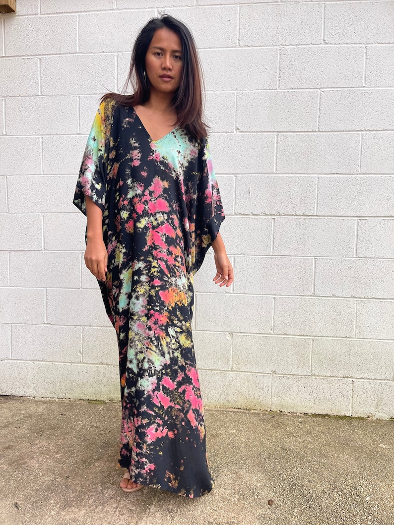 May include: A long black maxi dress with a tie-dye pattern in shades of pink, blue, and yellow. The dress has a V-neck and a relaxed fit.