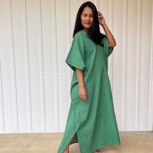 May include: A long, flowing green dress with wide sleeves and a V-neck. The dress has a relaxed fit and a slit on the side. The text "HALA handwork" and "Hollywood, MD" is visible on the left side of the image.
