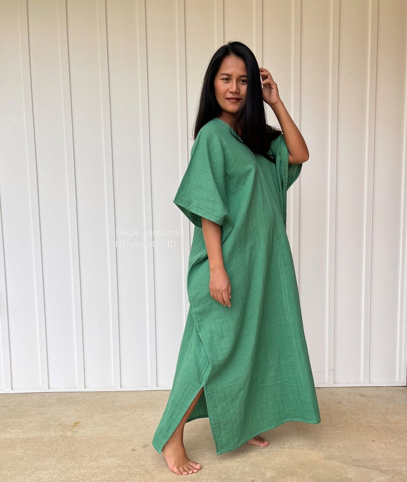 May include: A long, flowing green dress with wide sleeves and a V-neck. The dress has a relaxed fit and a slit on the side. The text "HALA handwork" and "Hollywood, MD" is visible on the left side of the image.