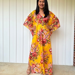 May include: A yellow maxi dress with a floral print. The dress has a V-neckline and 3/4 sleeves. The dress is made of a lightweight fabric and has a relaxed fit.