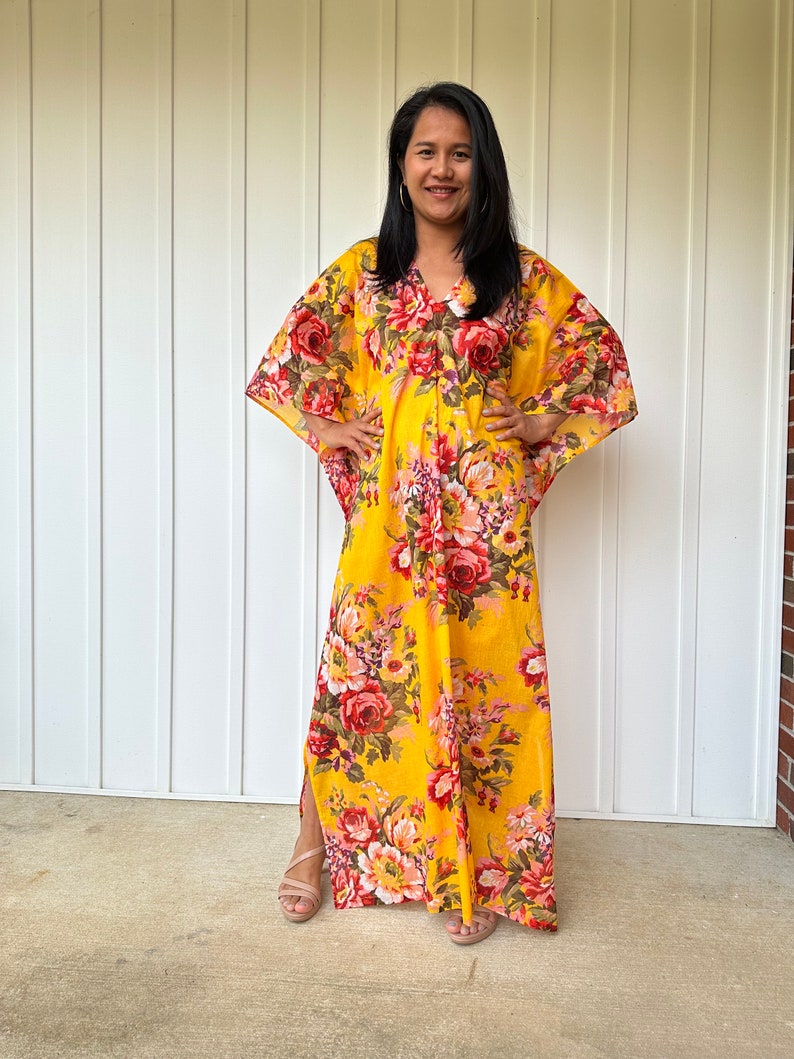 May include: A yellow maxi dress with a floral print. The dress has a V-neckline and 3/4 sleeves. The dress is made of a lightweight fabric and has a relaxed fit.