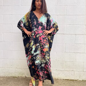 May include: A long black maxi dress with a tie-dye pattern in shades of pink, yellow, and blue. The dress has a V-neck and a relaxed fit.