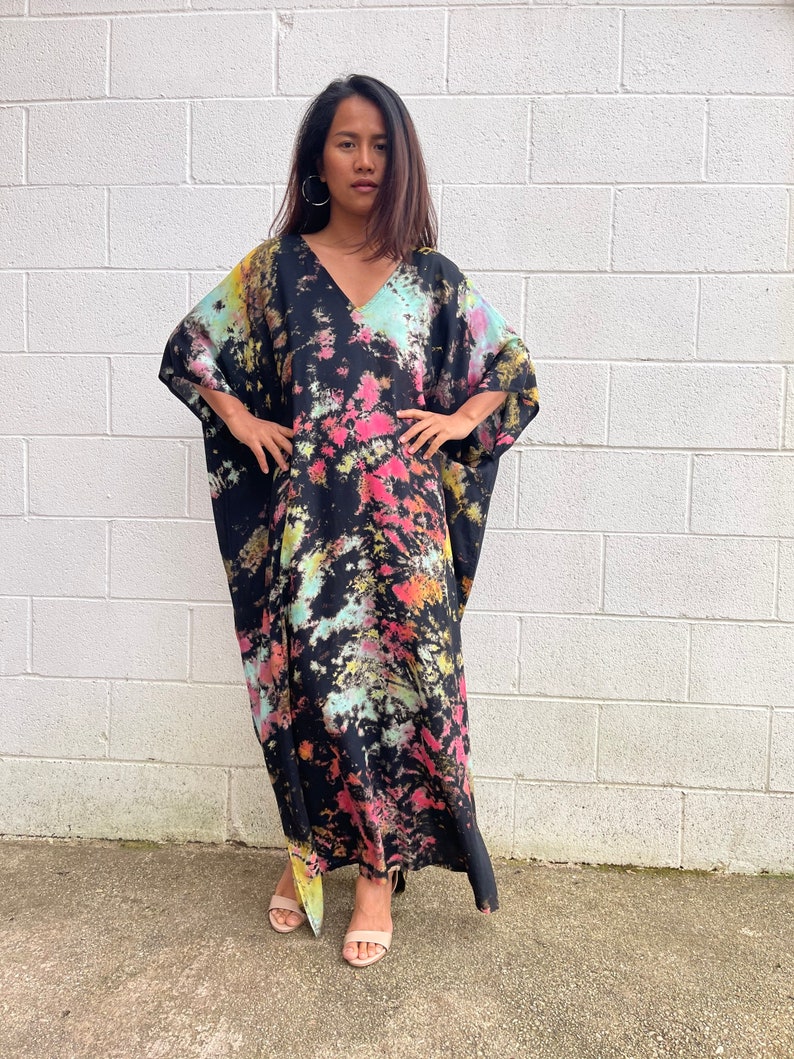 May include: A long black maxi dress with a tie-dye pattern in shades of pink, yellow, and blue. The dress has a V-neck and a relaxed fit.