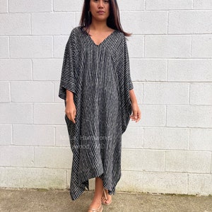 K&ouml;nnte beinhalten: Ein schwarz-wei&szlig; gestreiftes Kaftan mit V-Ausschnitt. Der Kaftan ist aus einem leichten Stoff gefertigt und hat eine flie&szlig;ende Silhouette. Das Model tr&auml;gt den Kaftan mit Sandalen.