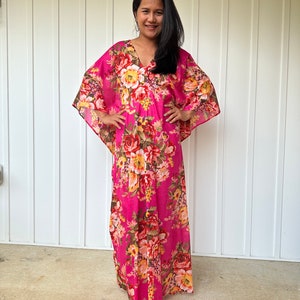 May include: A long pink maxi dress with a floral print. The dress has a V-neck and 3/4 sleeves.