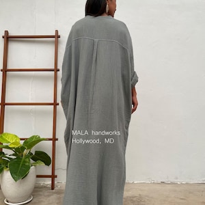 Pu&ograve; includere: Un lungo abito di cotone grigio, ampio e fluido, con bottoni sul davanti e maniche lunghe. L'abito &egrave; realizzato da MALA handworks a Hollywood, MD.