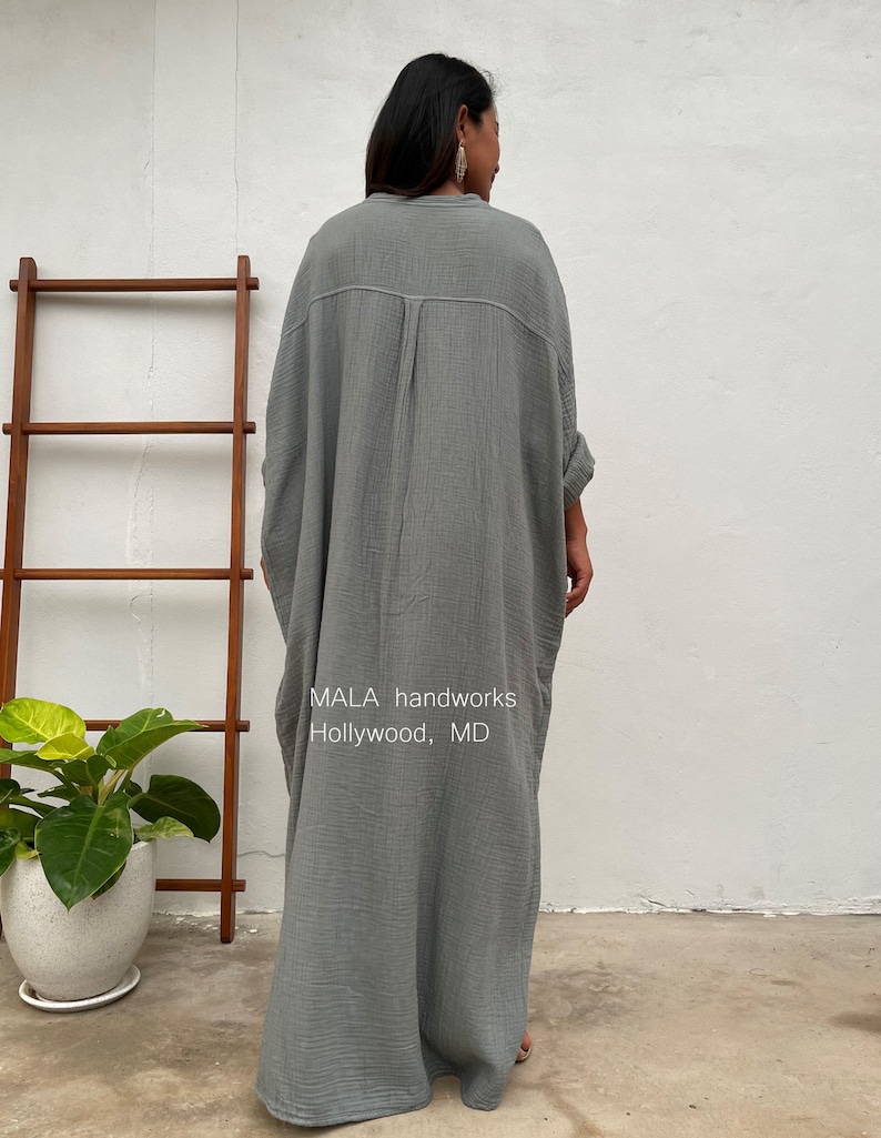 Pu&ograve; includere: Un lungo abito di cotone grigio, ampio e fluido, con bottoni sul davanti e maniche lunghe. L'abito &egrave; realizzato da MALA handworks a Hollywood, MD.