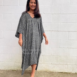 K&ouml;nnte beinhalten: Ein schwarz-wei&szlig; gestreiftes Kaftan-Kleid mit V-Ausschnitt und langen &Auml;rmeln. Das Kleid hat eine flie&szlig;ende Silhouette und einen leicht asymmetrischen Saum.