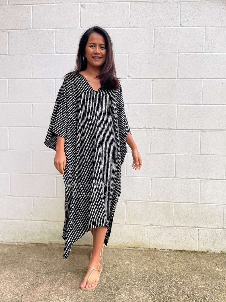 K&ouml;nnte beinhalten: Ein schwarz-wei&szlig; gestreiftes Kaftan-Kleid mit V-Ausschnitt und langen &Auml;rmeln. Das Kleid hat eine flie&szlig;ende Silhouette und einen leicht asymmetrischen Saum.