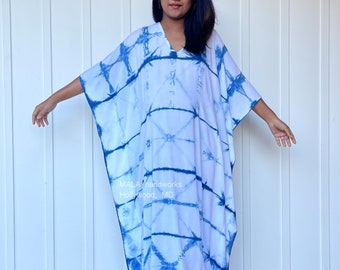 May include: A white and blue tie-dye kaftan with a V-neckline. The kaftan is long and flowing, and the tie-dye pattern is abstract and colorful. The text "MALA handworks Hollywood, MD" is printed on the front of the kaftan.
