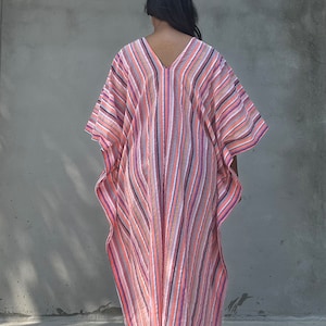 May include: A long, flowing, striped kaftan with a V-neckline. The kaftan is made of a lightweight fabric and has a relaxed fit. The colors of the stripes are pink, orange, white, and gray.