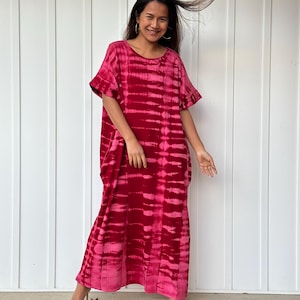 May include: A long, flowing red and pink tie-dye dress with a ruffled neckline and short sleeves. The dress is made of a soft, comfortable fabric and has a relaxed fit.