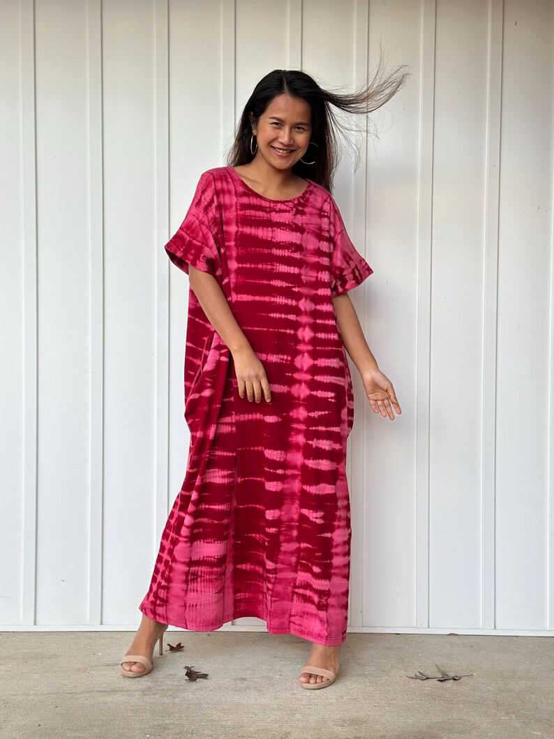 May include: A long, flowing red and pink tie-dye dress with a ruffled neckline and short sleeves. The dress is made of a soft, comfortable fabric and has a relaxed fit.