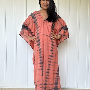 Peut inclure: Une longue kaftan de couleur corail fluide avec un motif tie-dye noir. La kaftan a un col en V et des manches longues.