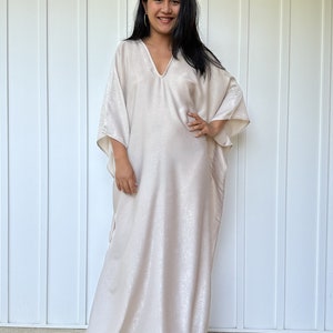 May include: A long, flowing, white kaftan with a V-neckline. The kaftan is made of a soft, silky fabric and has a relaxed fit.