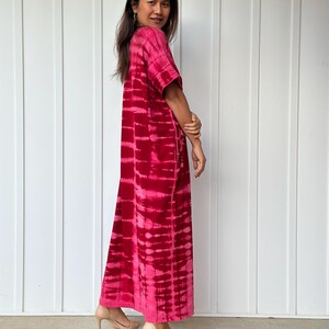 May include: A long, pink and white tie-dye maxi dress with short sleeves. The dress is made of a soft, flowing fabric and has a relaxed fit.