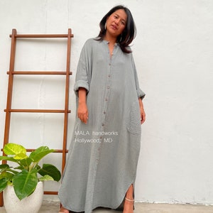 Pu&ograve; includere: Un lungo abito camicia grigio con bottoni e una tasca sul lato sinistro. L'abito ha una vestibilit&agrave; rilassata ed &egrave; realizzato in un tessuto morbido e confortevole. Il testo "MALA handworks Hollywood, MD" &egrave; stampato sul davanti dell'abito.