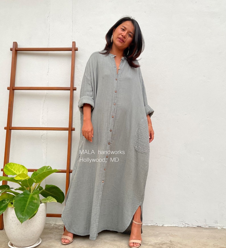 Pu&ograve; includere: Un lungo abito camicia grigio con bottoni e una tasca sul lato sinistro. L'abito ha una vestibilit&agrave; rilassata ed &egrave; realizzato in un tessuto morbido e confortevole. Il testo "MALA handworks Hollywood, MD" &egrave; stampato sul davanti dell'abito.