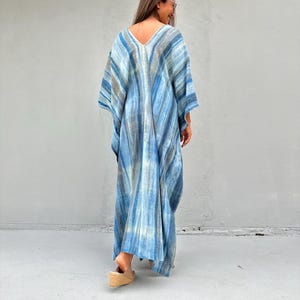 Puede incluir: Un vestido largo y fluido de kaft&aacute;n azul y blanco con estampado tie-dye y escote en V. El vestido est&aacute; hecho de una tela ligera y tiene un corte holgado.