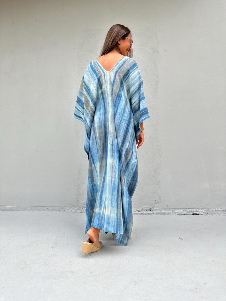 Puede incluir: Un vestido largo y fluido de kaft&aacute;n azul y blanco con estampado tie-dye y escote en V. El vestido est&aacute; hecho de una tela ligera y tiene un corte holgado.