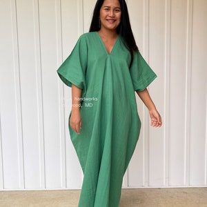 May include: A long, flowing green dress with a V-neck and wide sleeves. The dress is made of a soft, lightweight fabric and has a relaxed fit. The text "MA_ handworks" and "Highwood, MD" is visible on the dress.