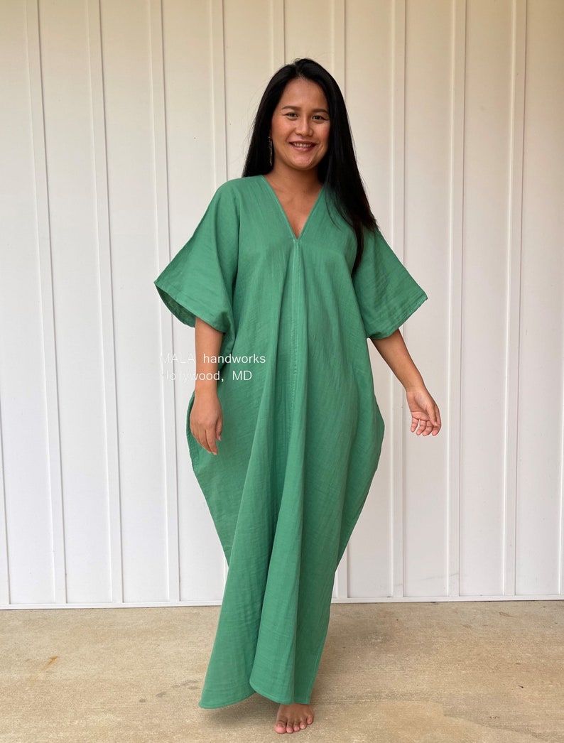May include: A long, flowing green dress with a V-neck and wide sleeves. The dress is made of a soft, lightweight fabric and has a relaxed fit. The text "MA_ handworks" and "Highwood, MD" is visible on the dress.