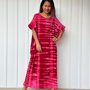 May include: A long, flowing pink and red tie-dye maxi dress with a ruffled neckline and short sleeves. The dress is made of a soft, comfortable fabric and has a relaxed fit.