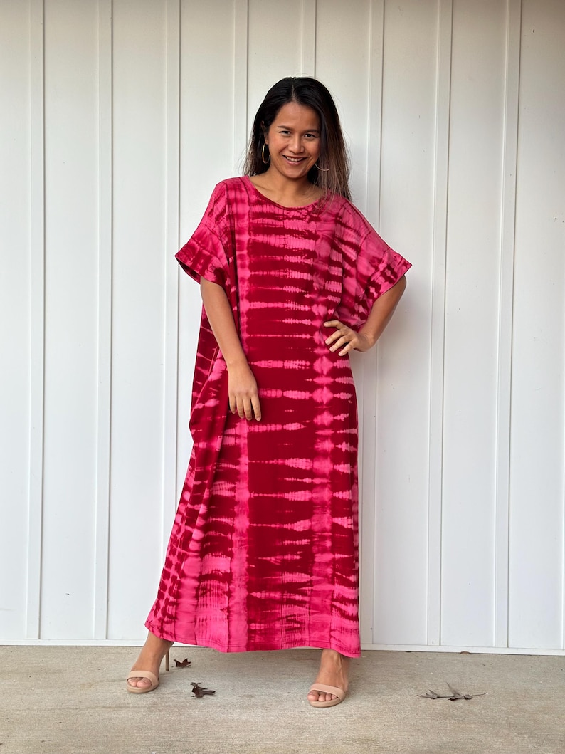 May include: A long, flowing pink and red tie-dye maxi dress with a ruffled neckline and short sleeves. The dress is made of a soft, comfortable fabric and has a relaxed fit.